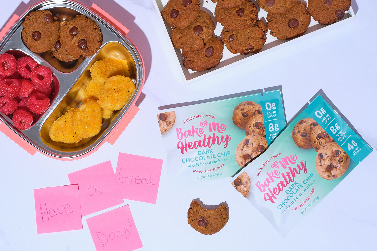 Bake Me Healthy Dark Chocolate Chip Cookies in a lunchbox with raspberries and chicken nuggets on a table